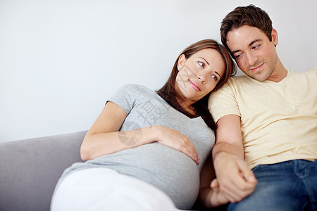 快乐的年轻怀孕夫妇坐在沙发上 在家放松休息时 - 是的 是的图片