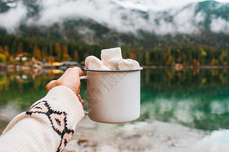 在德国巴伐利亚山脉里 与湖边的可可和棉花麦片杯子握手 森林背景公园溪流早餐咖啡饮料野餐巧克力叶子岩石食物图片