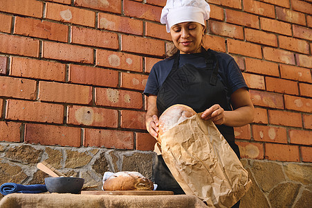 迷人的女面包师 工匠面包店的店员 用生态袋包装新鲜的酵母小麦面包 待售图片