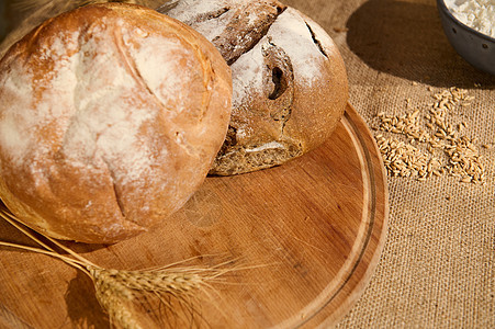 木板上各种新鲜烤面包的味道 零散的谷物和花边桌布上的小麦耳朵图片