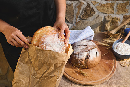 在手工面包店将传统自制酵母面包装入生态纸袋的特写图片
