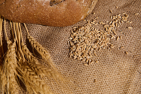 选择性地关注小麦金粒子旁边的燕麦谷 部分观看卷毛桌布上的酸瓜面包图片
