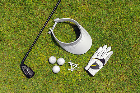 高尔夫球场绿草上高尔夫设备的顶视图 平躺的高尔夫球杆 球 手套 T 恤和帽子图片