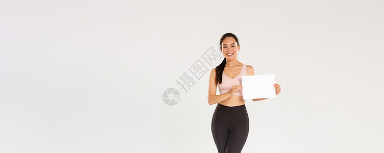 全长微笑漂亮的亚洲黑发女运动员 穿着运动服的女运动员在空白纸上展示标志 广告健身房会员或健身器材特价肌肉标识运动健美横幅女性情绪图片