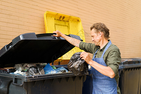 白种帅哥员工打开装满垃圾的罐子 用围裙扔塑料袋 错误的未分类垃圾桶 扔垃圾的错误方式 垃圾分类拯救世界图片