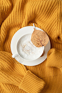 黄色毛衣上方的卡布奇诺咖啡杯图片