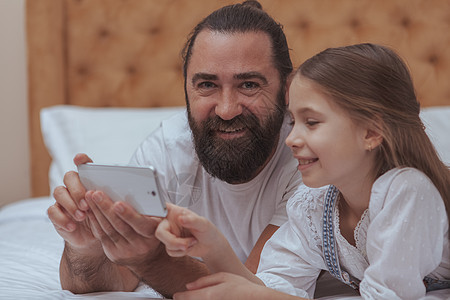 父亲和女儿在家里享受舒适的一天父母童年孩子们视频爸爸电话孩子手机单身闲暇图片