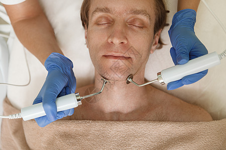 成熟男子在美容诊所接受面部皮肤护理治疗仪器男性刺激中年化妆品休息美容师电解皮肤科胶原背景图片