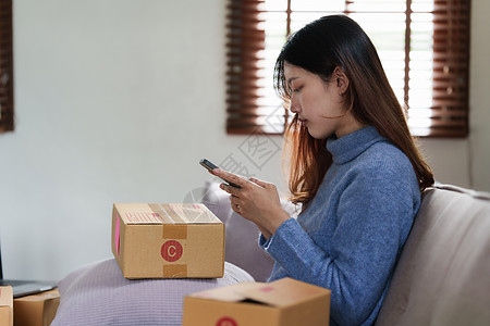 年轻亚裔女性与朋友聊天 透过智能手机在沙发上观摩社交媒体的肖像 坐在沙发上长椅细胞公寓屏幕电影技术休息展示男人程序图片