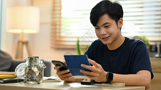 快乐的亚洲年轻人使用智能手机进行在线支付 在客厅管理费用财务图片