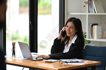 手持笔记本电脑和在移动电话上说话的女性创业者微笑图片