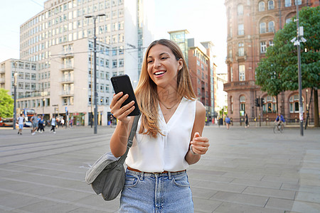 在英国曼彻斯特市看她的智能手机行走的女积极商业妇女图片