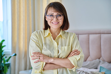 自信的中年妇女在家庭室内看着相机的肖像双臂成人头发女性享受牙齿快乐房间双手微笑图片