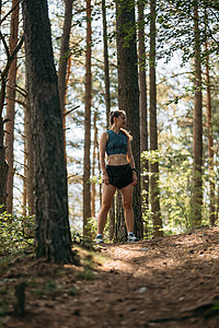 身穿运动服的年轻女跑运动员站在绿色森林的足迹上 在准备马拉松时准备逃跑图片