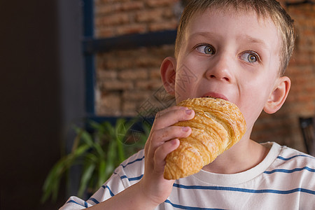 男孩在咖啡馆吃羊角面包的肖像 特闭店 复制文本空间图片