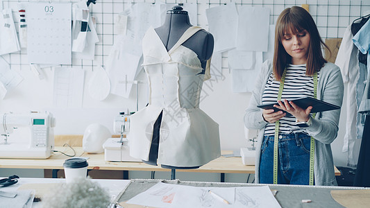 年轻的时装设计企业家正在使用平板电脑 同时检查固定在裁缝假人身上的衣服 服装制造概念中的现代技术制造业手工工艺生意模型商业职业工图片