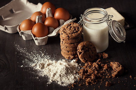 巧克力饼干在生锈木制桌子上 配有牛奶 白面粉 新鲜鸡蛋 奶油和碎屑小吃糕点早餐葡萄干芯片食物蛋糕乡村棕色面包屑图片