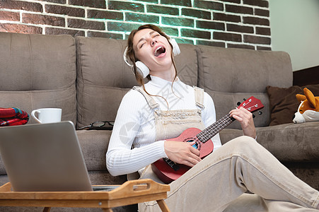 远程音乐课 玩呼乐或教歌声 唱歌 在客厅坐在地板上时 一流学生用笔记本电脑网络摄像头录制或学习图片
