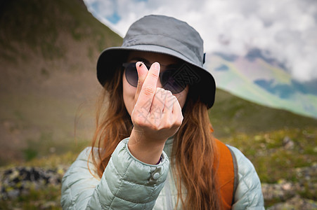 在落基山脉和云彩的背景下 一位面带微笑 积极向上的年轻女性的肖像 用手指展示了一只苍蝇坐着的现代心形手势 既有趣又有趣图片