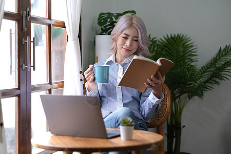 亚洲妇女看书和在家喝咖啡放松自 己的亚洲妇女女孩头发微笑杯子图书馆咖啡食物艺术窗户早餐背景图片