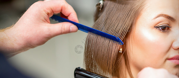 美发师在美容院用铁直发器和梳子将中等长度的女性棕色头发拉直造型发型梳妆台治疗女孩造型师护理理发客户女士图片