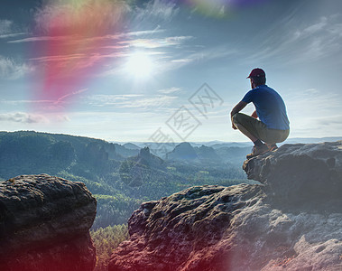 坐在山顶悬崖上看日出的人爬坡道岩石闲暇登山者石头寂寞运动阳光顶峰天空图片