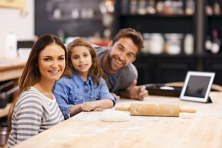 他们是一个吃货家庭 一个幸福的三口之家的肖像在厨房里一起烘烤 用数字平板电脑来帮助他们图片