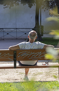 男人坐在公园的长椅上 在阳光明媚的日子放松图片