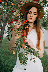 一个戴着帽子的漂亮金发女孩 留着长发 在秋季散步 一个女人在罗文树上的画像金发女郎裙子白色植被季节时间草帽浆果美甲自由图片