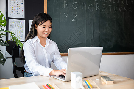 年轻女教师用笔记本电脑在课堂办公桌上的肖像女孩工作办公室女性互联网教学英语教授女士测试图片