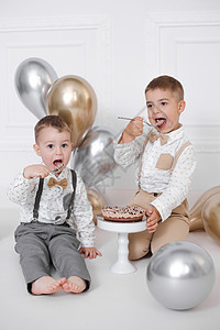 两个男孩庆祝生日 孩子们有一个 B 日派对 用蜡烛和气球的生日蛋糕 快乐的孩子们吃蛋糕 庆祝 白色简约的内饰喜悦工作室极简甜点金图片