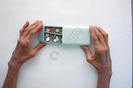 高龄妇女从白种背景的药丸盒中服用医用药丸背景图片