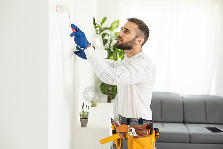 有油漆滚筒的男性手绘画墙壁 粉刷公寓 用白色油漆翻新工作装潢画家维修修理工梯子退休住宅房间工人图片