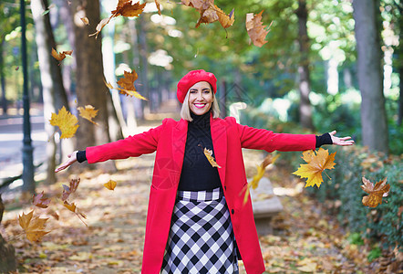快乐的女人在公园里丢落秋叶图片