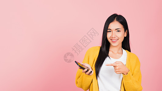 亚洲快乐的美丽年轻女子微笑 在网上购物申请中用手持手机指着智能手机时使用手指指尖女士相机黑发衬衫毛衣青少年技术屏幕女孩头发图片