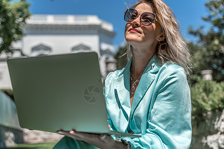 一位美丽的年轻女子 金发卷发戴眼镜 穿着蓝裙子 在大自然的草地上坐着 用笔记本电脑地面房间房子学生技术稻草女性手机自由职业者咖啡图片
