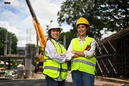 身穿安全头盔和反光夹克的建筑师女性双臂交叉站立在工业建筑施工现场图片