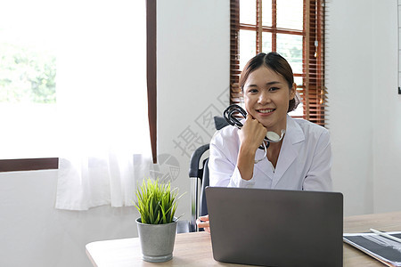微笑的亚裔女医生在她的办公室里拿着笔记本电脑 友好的医疗专业人员在诊所使用平板电脑保健从业者工作女性治疗女孩职员男人男性成人图片