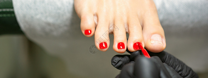 在美容院的女脚趾甲上 涂红指甲油的恋童癖病学温泉手套美容师服务修脚师程序皮肤凝胶毛巾图片
