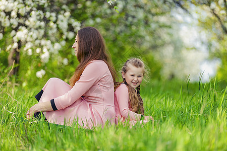 母亲和女儿在大自然中互相背对背地坐在一起公园农村父母女性孩子乡村童年裙子家畜晴天图片