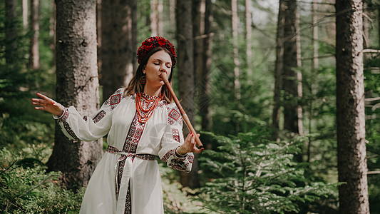 在木管乐器木笛上演奏的年轻女子-森林背景下的乌克兰特伦卡或泰林卡 民间音乐概念 乐器 传统刺绣衬衫的音乐家图片