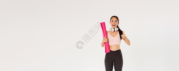 全长快乐 满意 苗条的亚洲女孩 戴着健身橡胶垫和耳机 女运动员竖起大拇指 推荐健身房或瑜伽课 锻炼后看起来很高兴广告运动成人健美图片