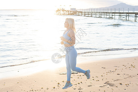 年轻漂亮的运动女孩在日出时 在海边上训练公园成人海洋女士日落跑步天空运动员慢跑者海滩图片
