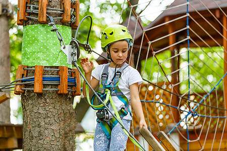 可爱的小女孩在温暖阳光明媚的夏日 享受她在攀登冒险公园的时间女孩森林头盔耳环力量挑战绳索运动活动冒险图片