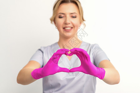 一个微笑的天主教女医生 穿着粉红色手套 身着制服 在白色背景下 展示了心脏的象征物诊所手指保健胰腺药品生活治疗疾病卫生女士图片