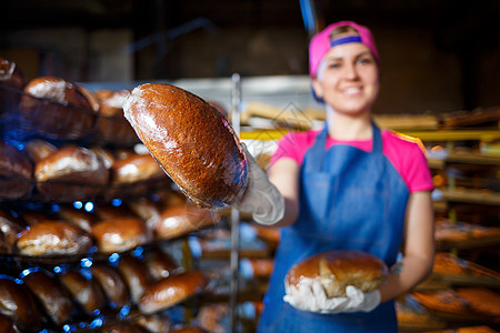 微笑的面包师女孩围裙拿着面包 看着相机 少妇是拿着新鲜的烘烤的厨师 一个欧洲人长相的快乐女孩正在面包店微笑幸福服务员乐趣产品工人图片