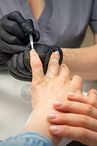 画女性指甲 戴着黑色手套的美甲师的手正在美甲沙龙的女性指甲上涂上透明指甲油护理魅力治疗客户奢华美容师身体化妆品手指凝胶图片