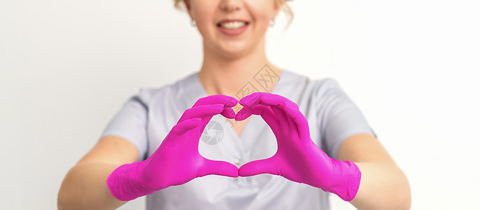 一个微笑的天主教女医生 穿着粉红色手套 身着制服 在白色背景下 展示了心脏的象征物药品外科感染安全医师医院乳胶保健临床职业图片