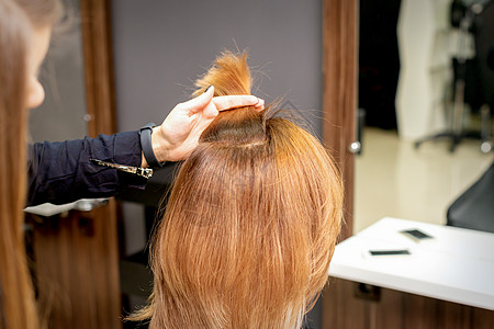 美发师在女性头发的手指间握着一根线 在美发沙龙检查年轻女子的头发工作治疗顾客女孩理发发型手臂造型师梳子职业图片