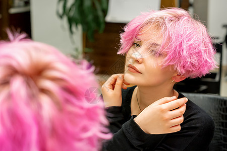 美丽的年轻白种女人 留着新的粉红色短发型 在美发沙龙的镜子里看着自己的倒影 检查发型理发卷曲反射护理治疗成人头发女孩女士化妆品图片